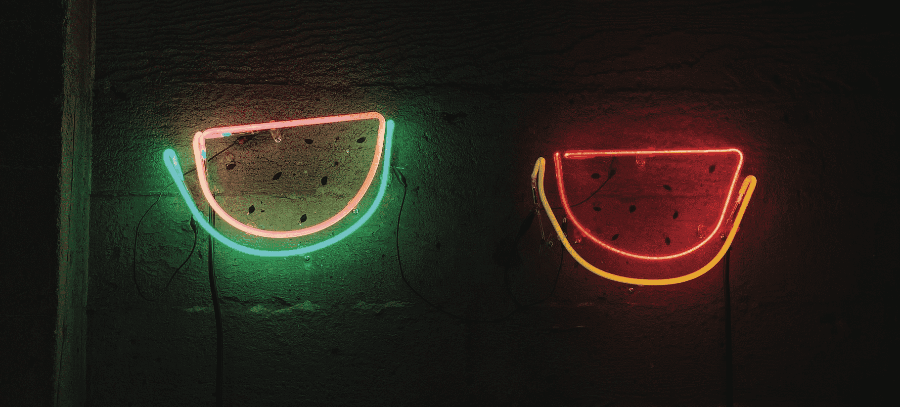 Two lit-up neon watermelons, one on the left with a green exterior and pink interior, and the other on the right with a yellow exterior and red interior. 