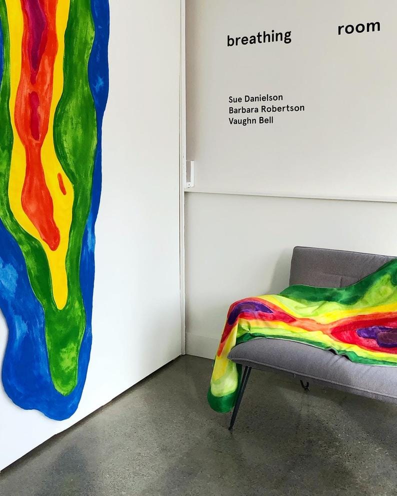 A hanging rainbow blanket and another rainbow blanket on a couch; a sign above that says 