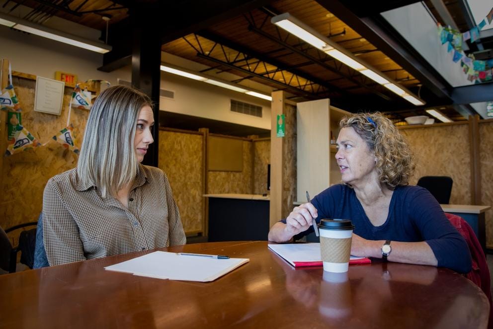 Stacey Marron and Kelsey Fleetwood talk at a wooden table 