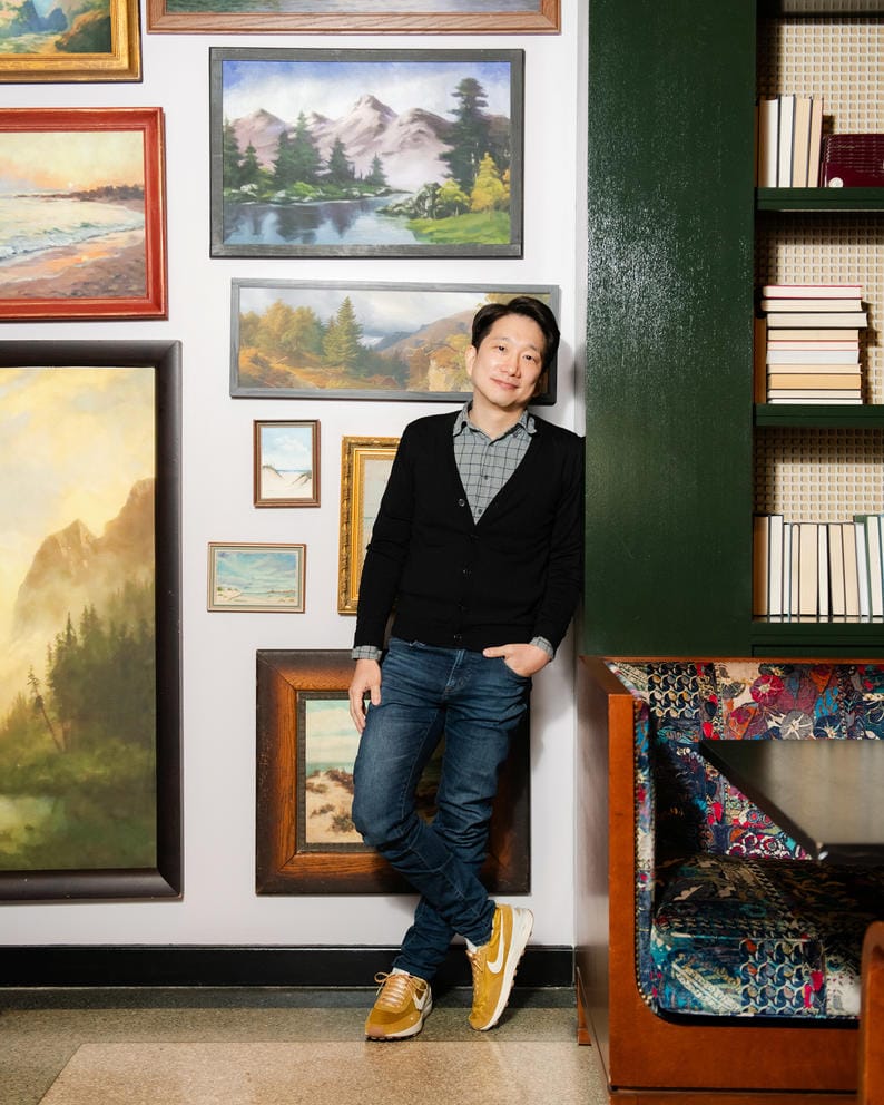 A person poses for a photo in front of landscape art and books