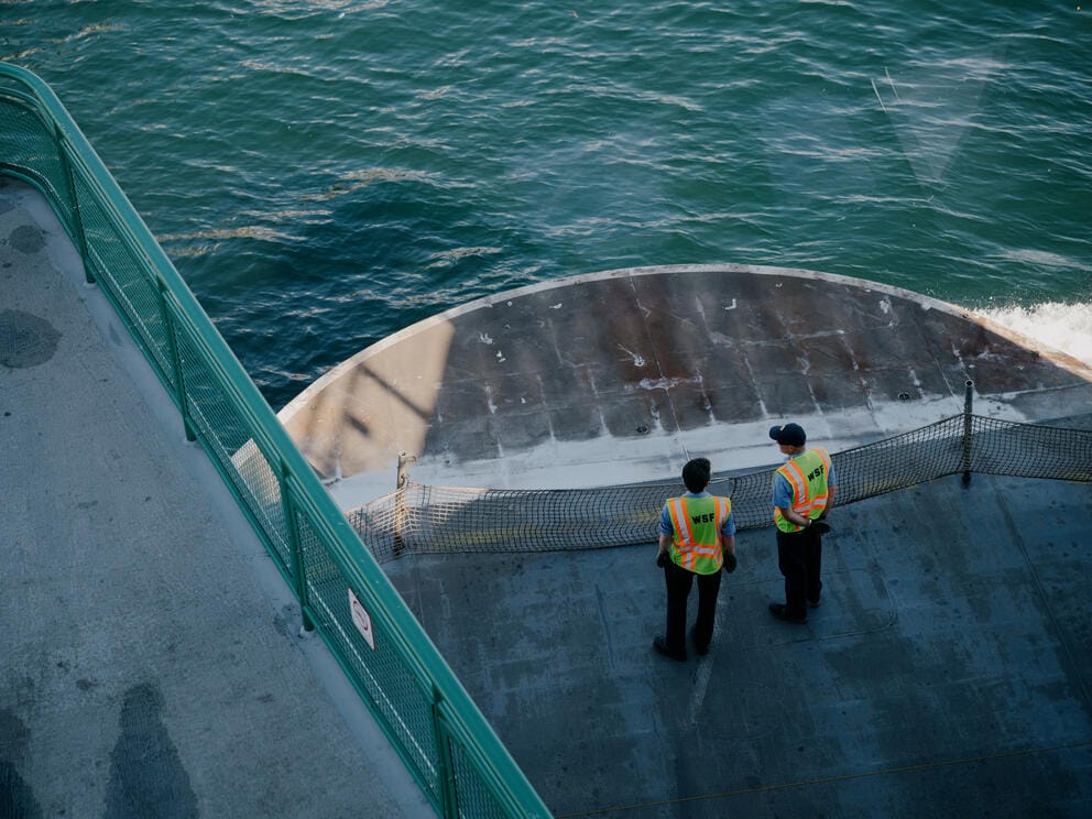 Two deck hands in bring colors stand at the front of a ferry.