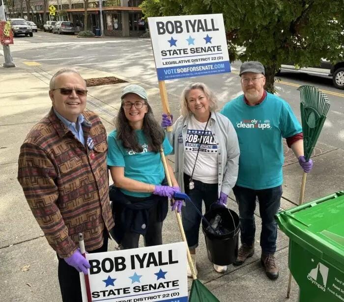Four people pose for a photo outside, holding campaign signs that say