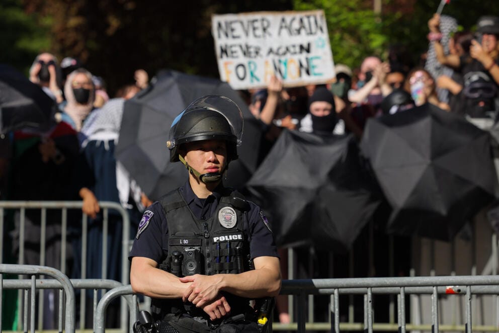 A police officer in protective gear stands in front of a crowd barricade and protesters