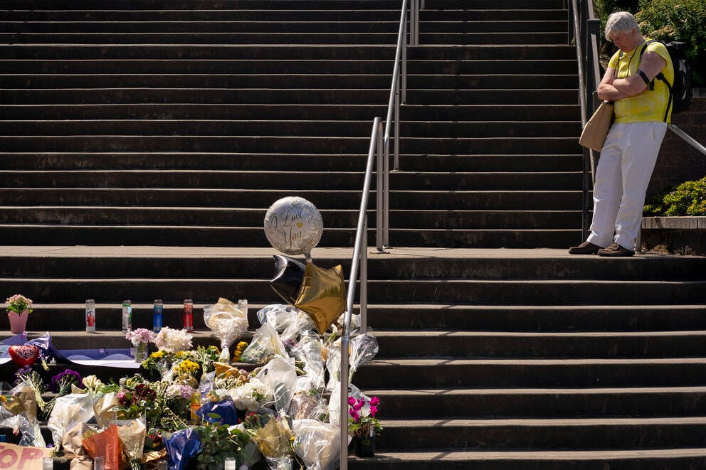 A man stands on a set of stairs next to a memorial full of flowers and balloons