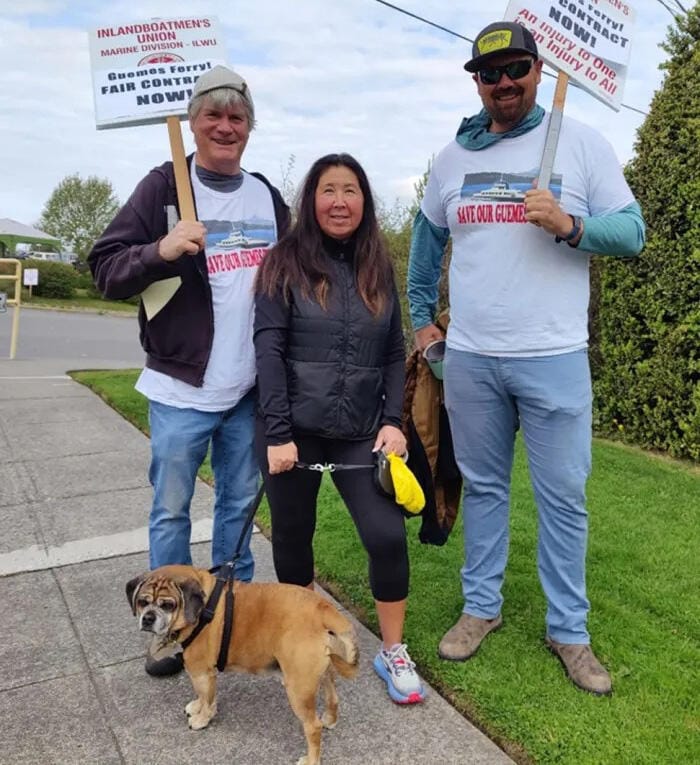 Three people pose for a photo outside holding signs that say,