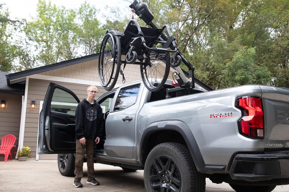 A man loads a wheelchair into the a truck bed.