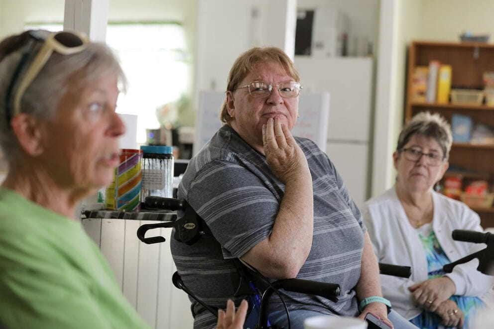 Three residents sit in discussion in a mobile home park clubhouse