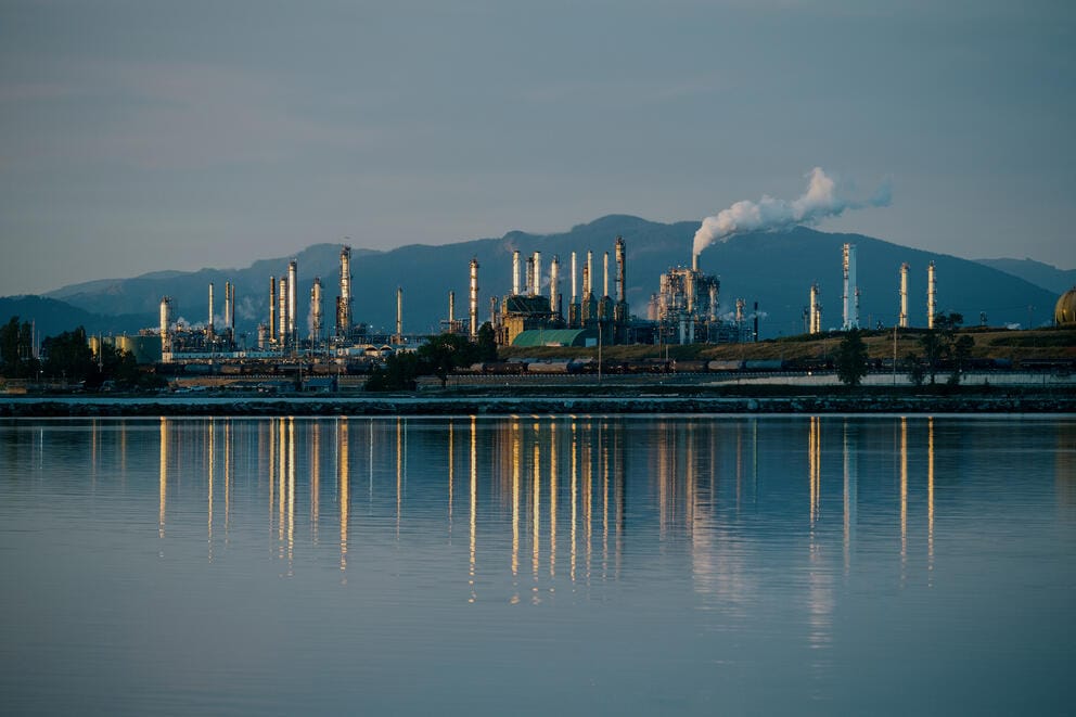 An oil refinery is reflected from across the water at dusk