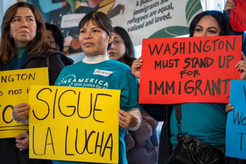 Protesters hold signs in Spanish saying 