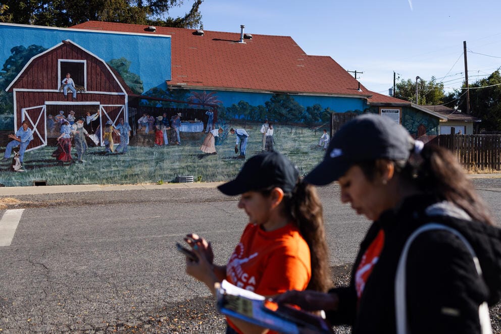 Canvassers walk by a mural 