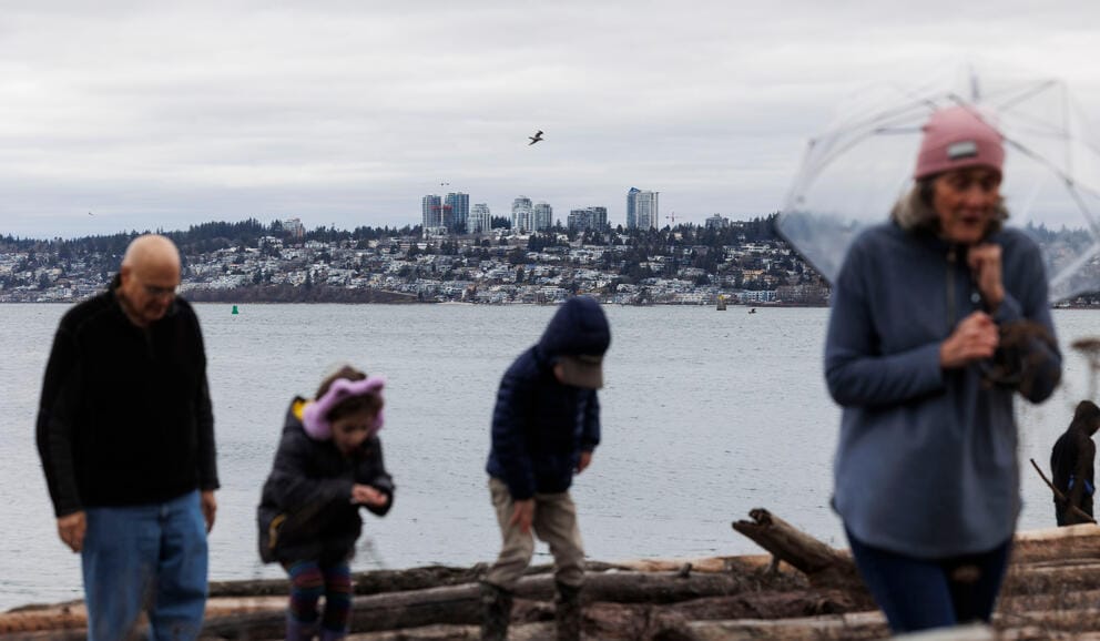 Four people walk away from water, and a skyline is seen in the background.