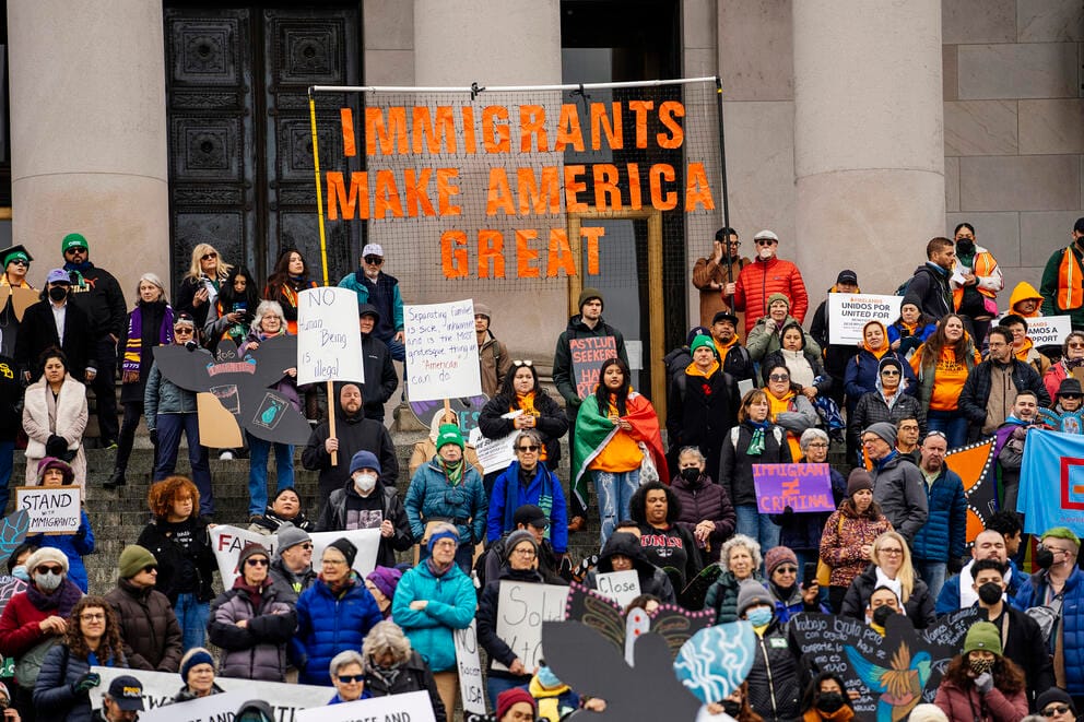 A group of people hold signs on steps, including one huge one that says