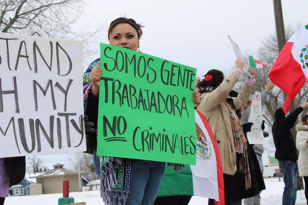 A person holds a green protest sign that says, 