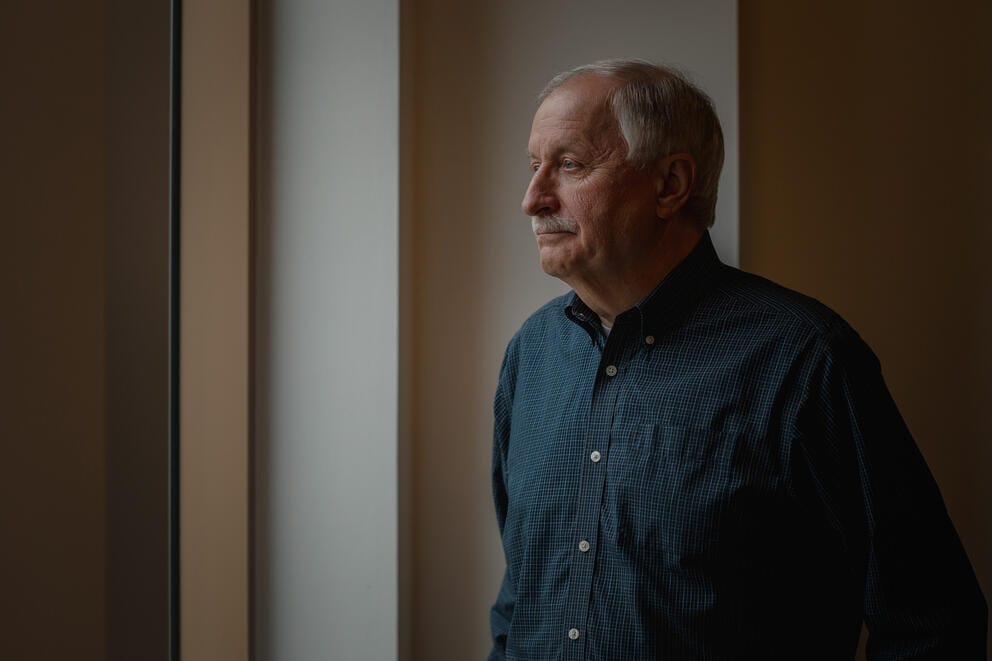a white man in a blue shirt stands for a portrait 