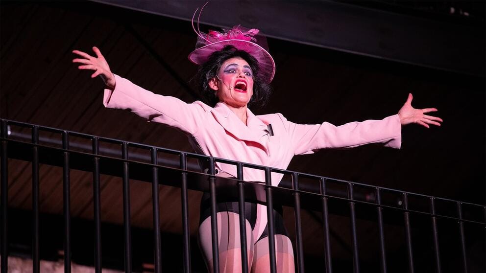 during a play, a woman in a Titanic-era costume throws her arms out while standing on a balcony